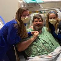 A photo of Ronald and a team of his nurses smiling for the photo from the side of his hospital bed.