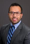 Headshot for Dr. Nakul Natyal from the chest up wearing a grey jacket and blue shirt and striped blue tie